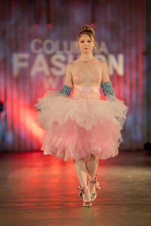 Pink tulle tutu dress with ruffled layers shown on fashion runway with dramatic red lighting.