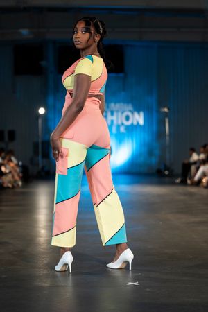Model showcases colorful geometric patterned jumpsuit in coral, yellow and turquoise during fashion week event.