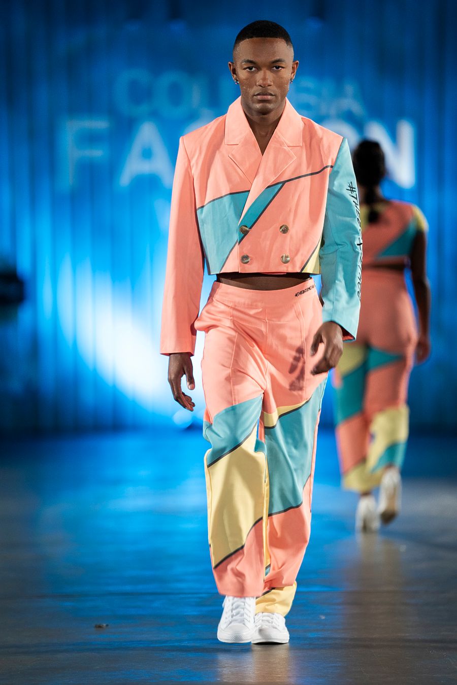 Model presents color-blocked pastel suit in coral, blue and yellow at fashion show.