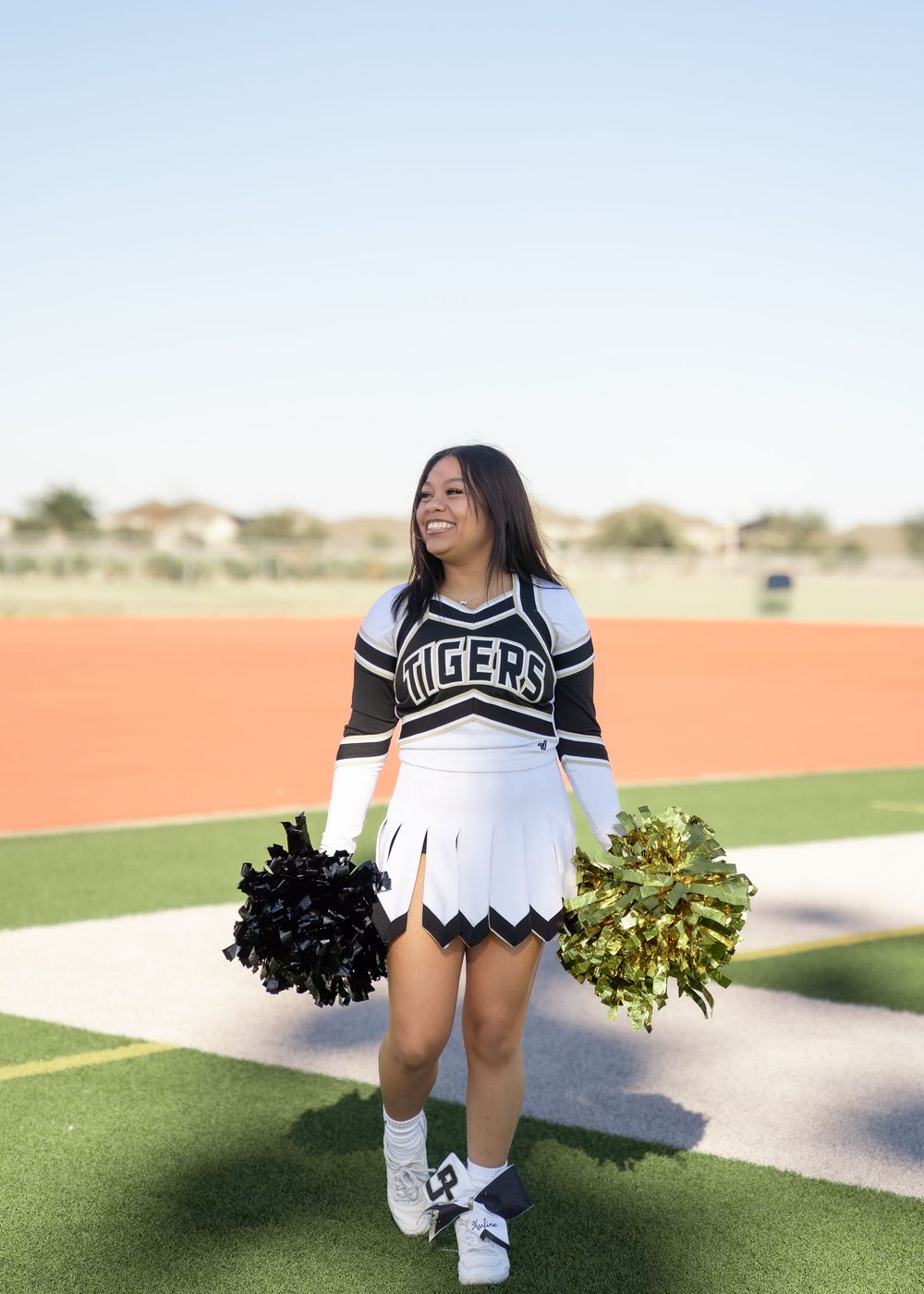 CyPark High cheerleader posing on football field with pom-poms, smiling in uniform