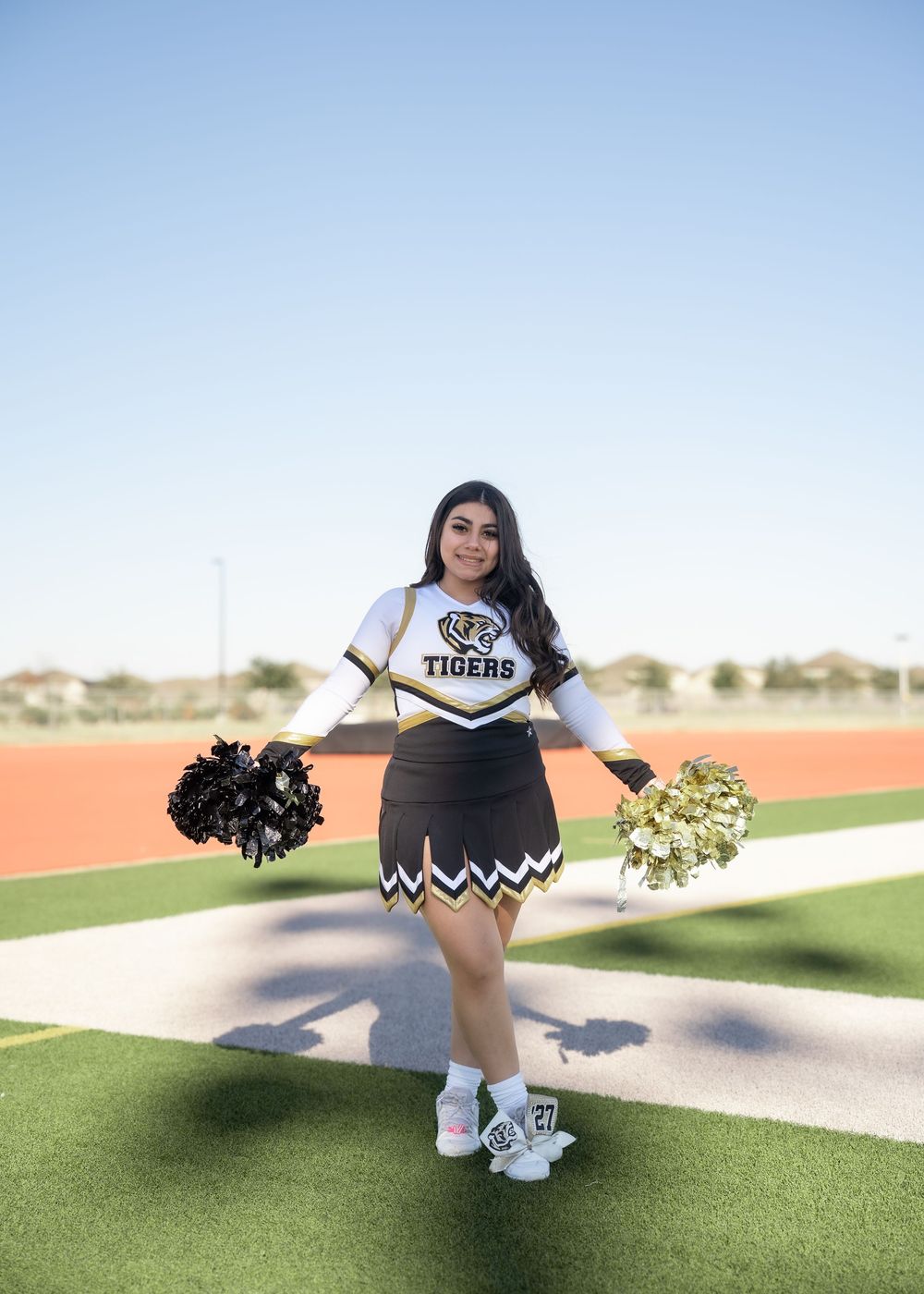 CyPark High cheerleader posing on football field with pom-poms, smiling in uniform