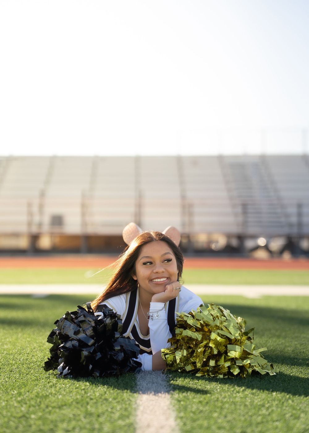 CyPark High cheerleader posing on football field with pom-poms, smiling in uniform