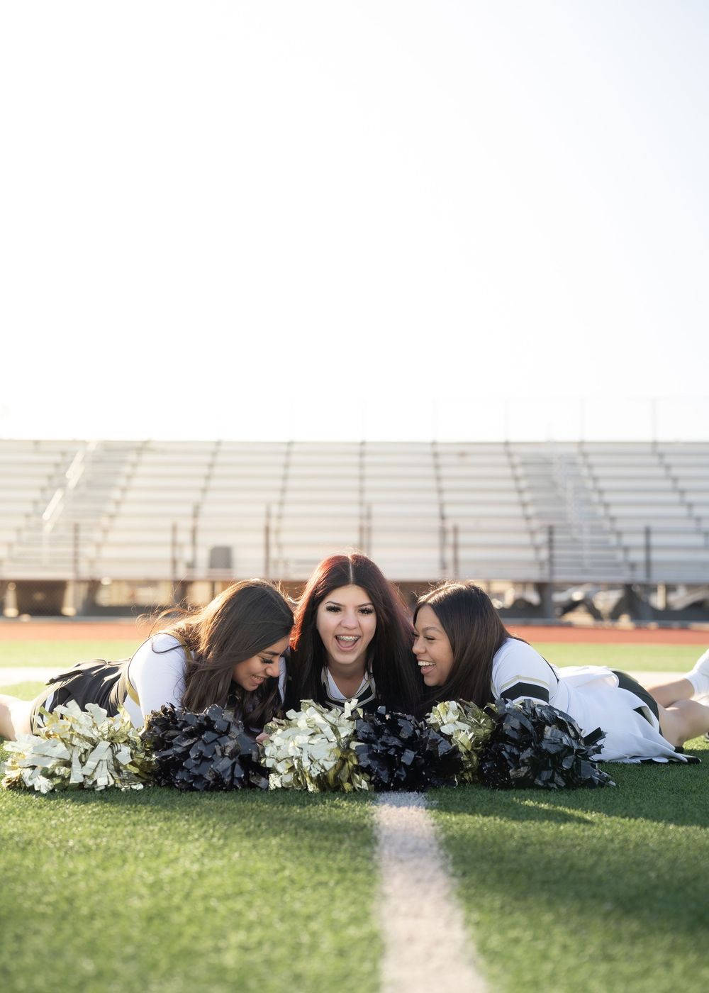 Three best friends in cheer uniforms laughing together on football field
