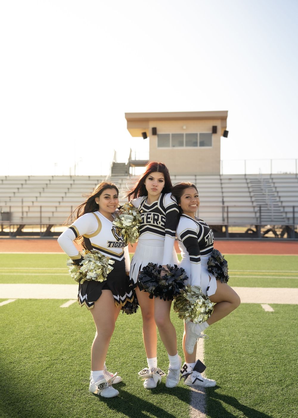 Three best friends in cheer uniforms laughing together on football field