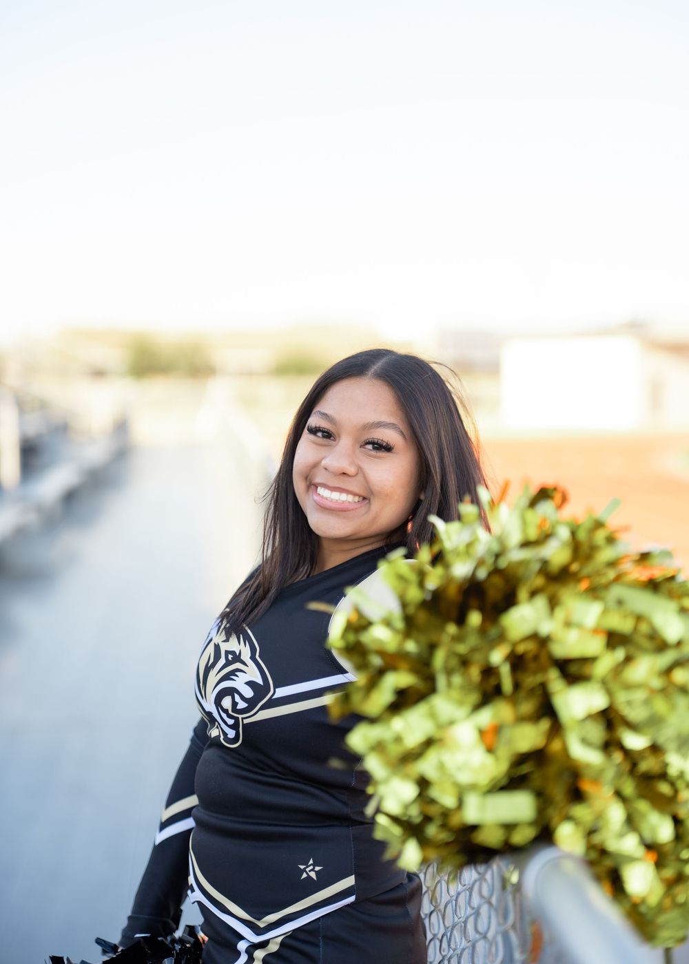 CyPark High cheerleader posing on football field with pom-poms, smiling in uniform