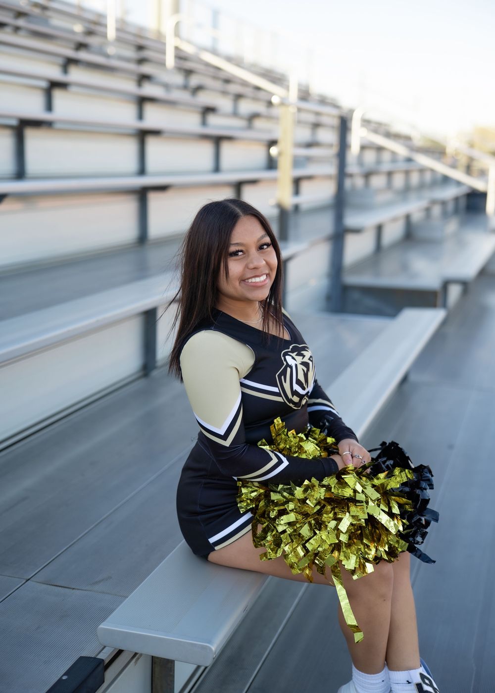 CyPark High cheerleader posing on football field with pom-poms, smiling in uniform