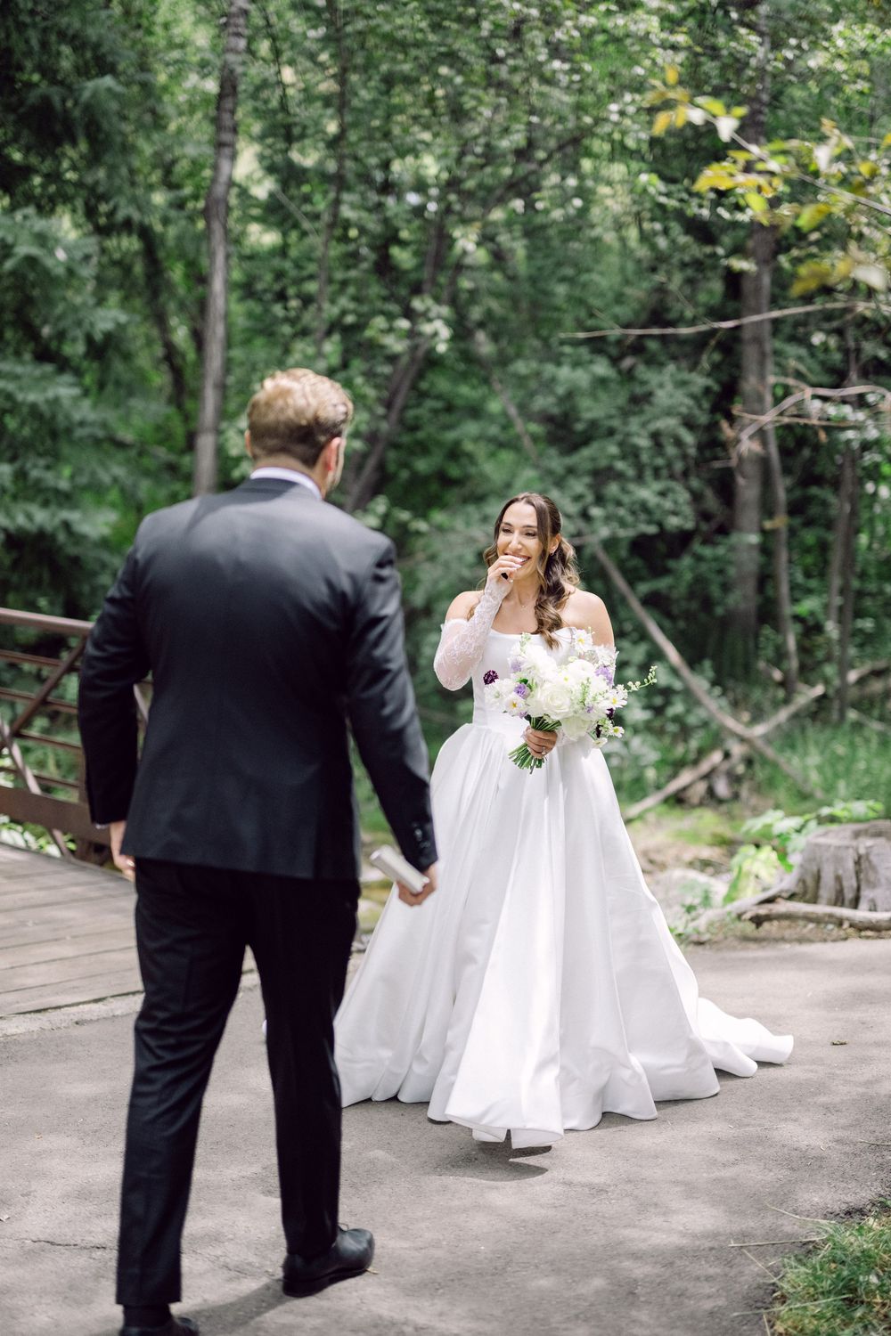 Wedding couple walking together on a woodland path surrounded by lush greenery.