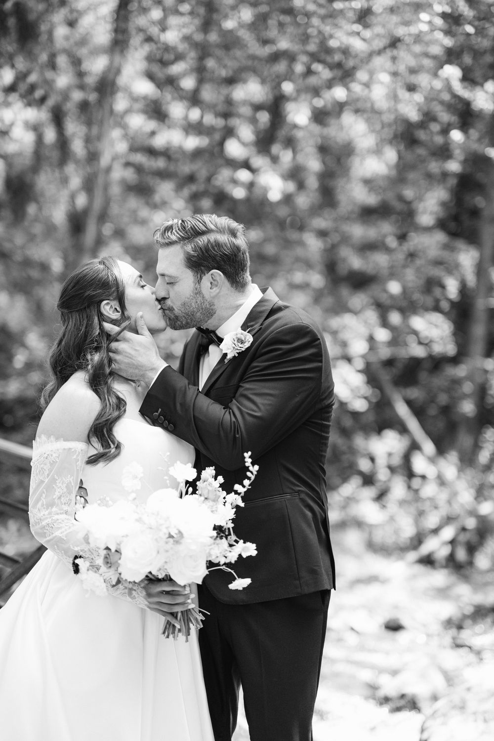 Black and white wedding portrait showing a romantic moment between newlyweds in a forest setting.