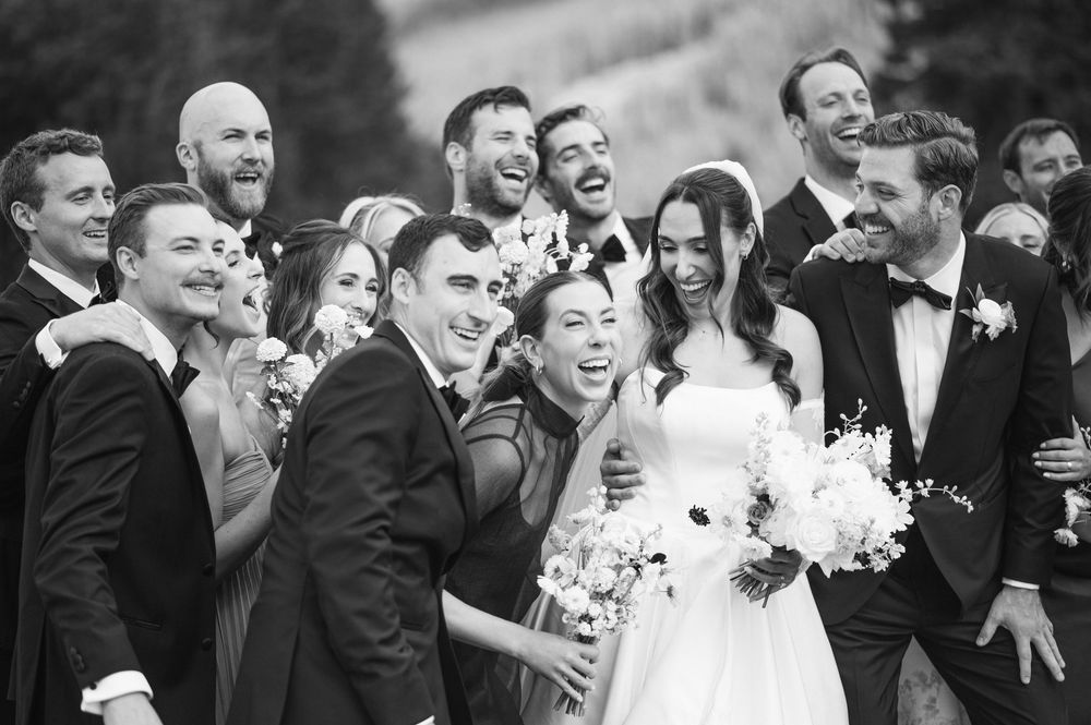 A candid black and white photo shows joyful wedding guests laughing together during a reception celebration.
