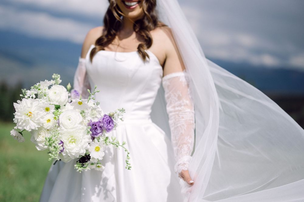 Bride's flowing white veil catches the breeze against mountain backdrop during outdoor wedding portraits.