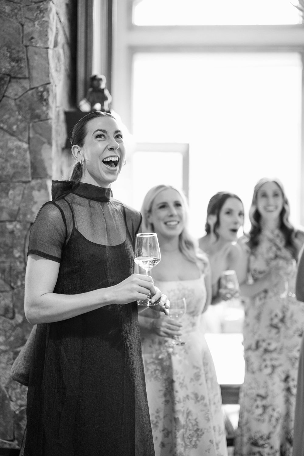 Wedding party members share joyful laughter during candid moments at an indoor reception venue.