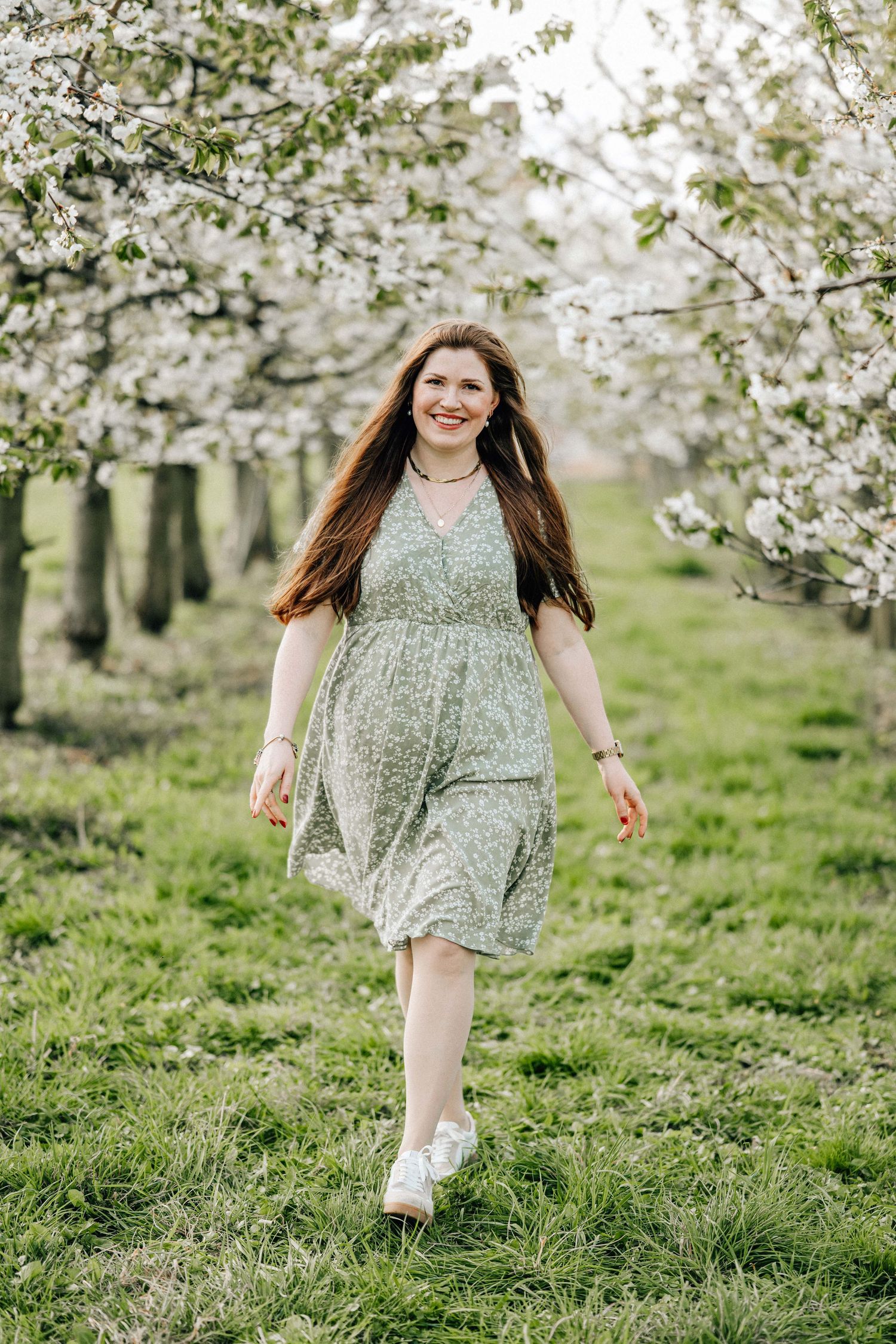 A person in a floral dress runs joyfully through a blooming spring orchard with white cherry blossoms.