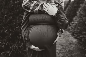 Black and white close-up of a pregnant woman's baby bump with partner's hands wrapped around her.