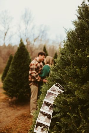 Ultrasound photo strip hanging on a Christmas tree with expecting couple kissing in background.