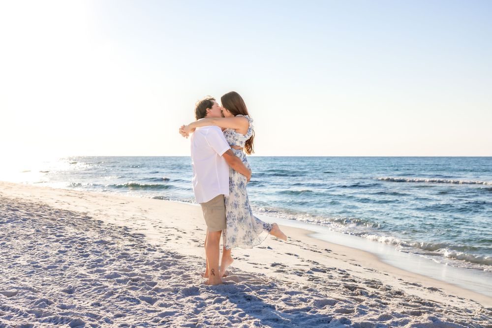 A couple shares a romantic moment on a sandy beach at sunset with the ocean waves in the background.
