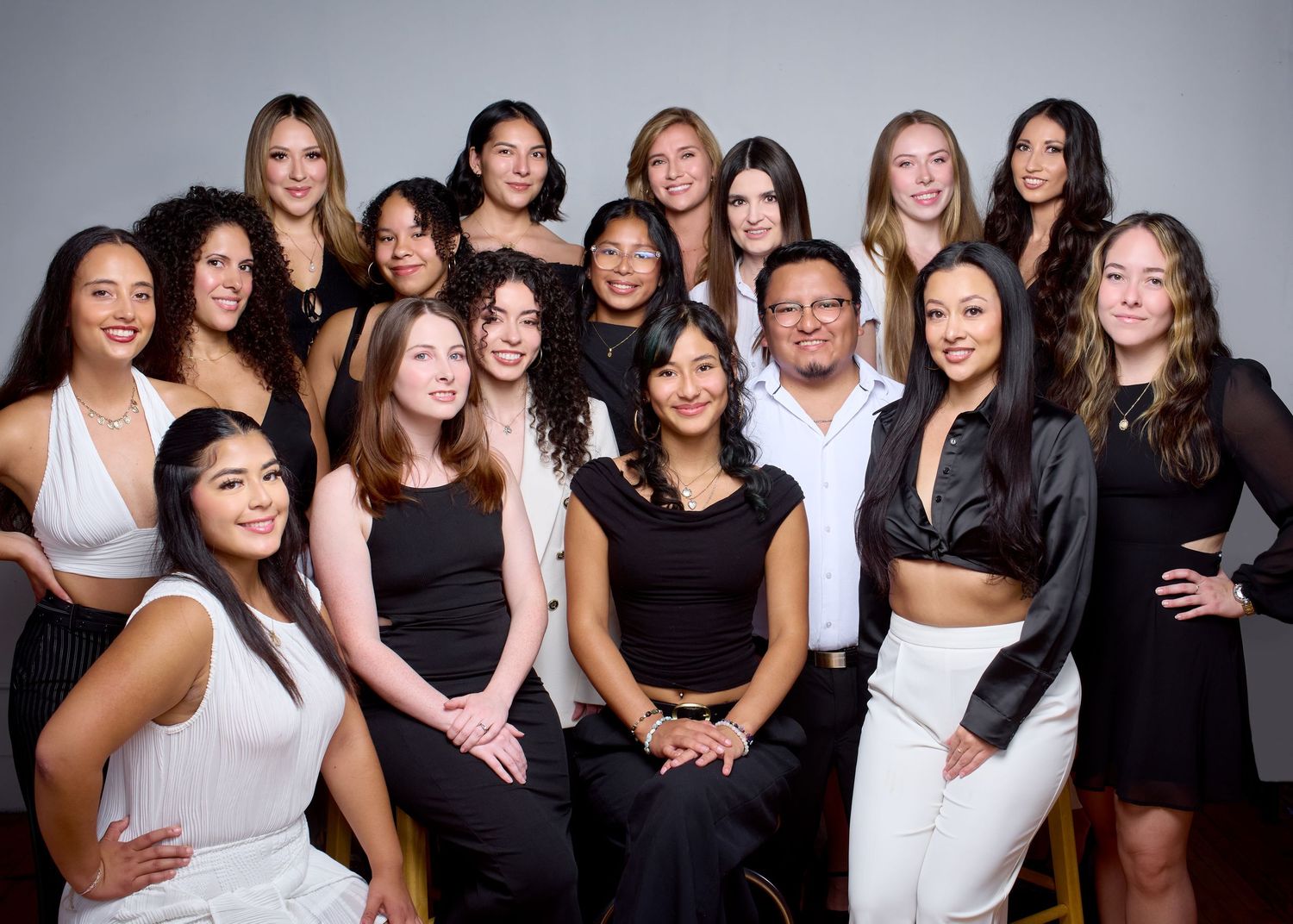 Diverse group of young women in black and white outfits posing with a man for a professional photo.