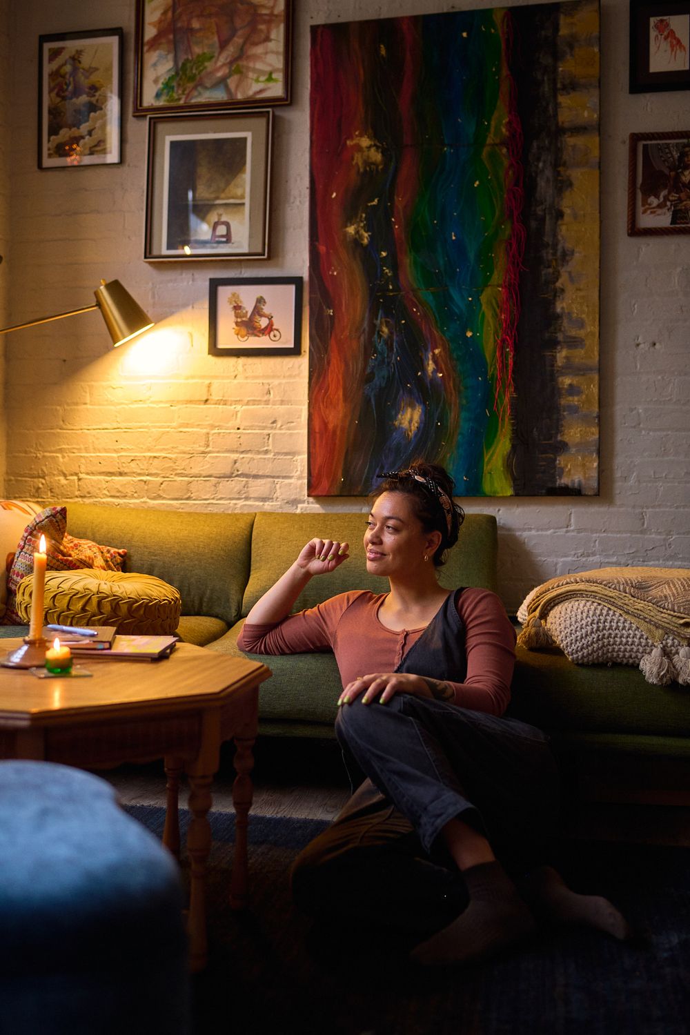 Woman relaxing on green sofa in cozy living room with colorful abstract art and warm lamp lighting.