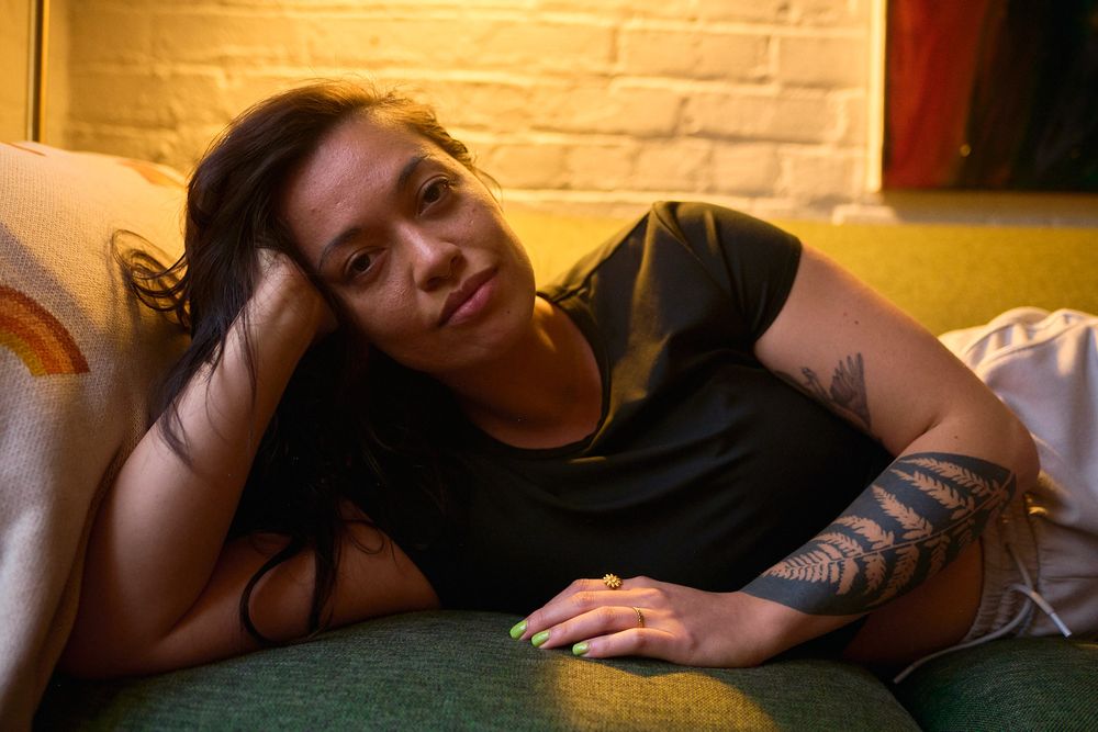 Tattooed woman lying on green sofa in warm golden light with relaxed expression.
