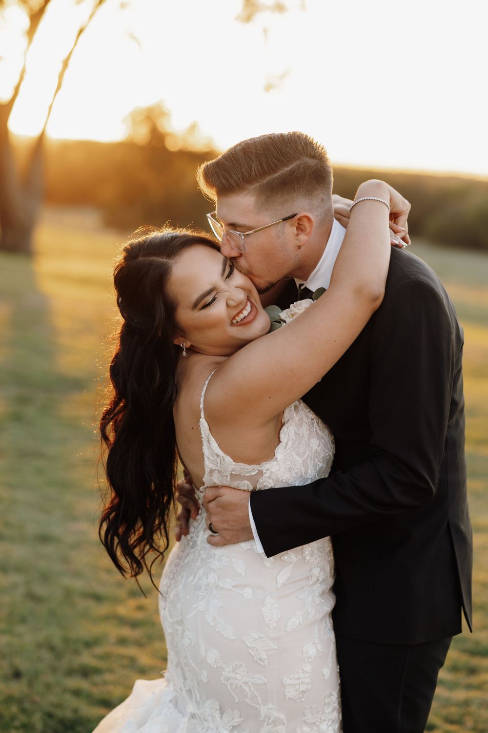 Romantic sunset wedding portrait of couple embracing in golden light on grassy field.