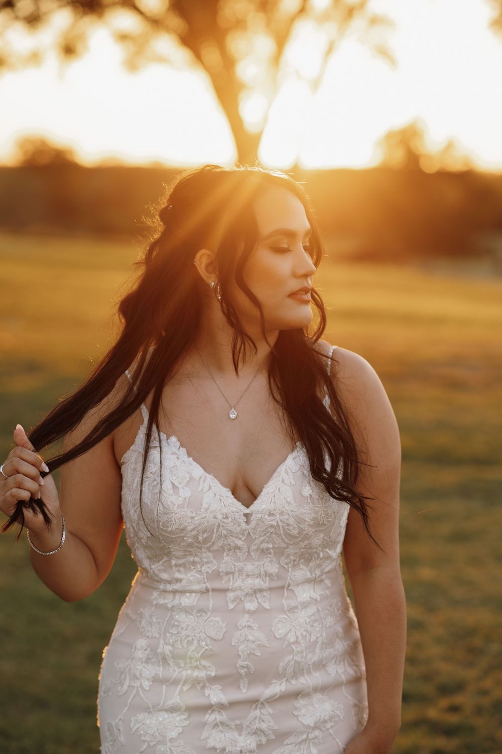 A person in a white lace wedding dress twirls in a golden sunset-lit field creating a dreamy outdoor portrait.