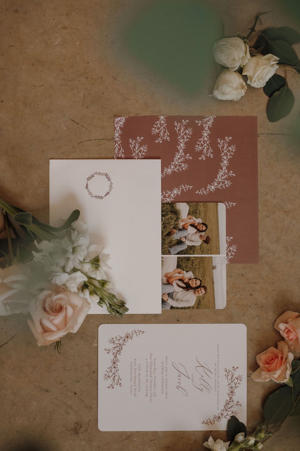 Elegant wedding invitation suite with delicate floral designs and pink roses on a rustic brown background.