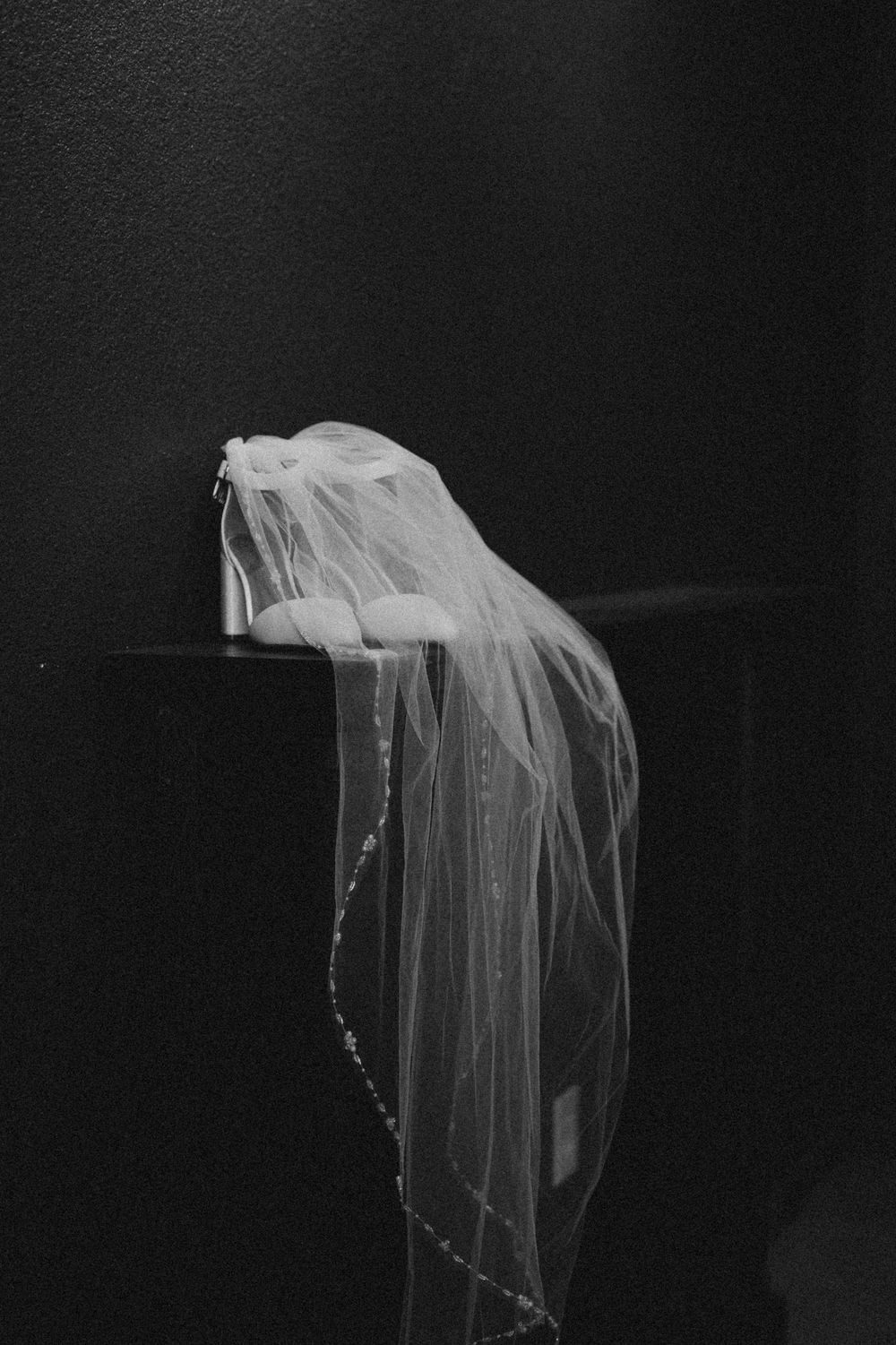 A delicate white wedding veil draped elegantly against a dark background in dramatic black and white.
