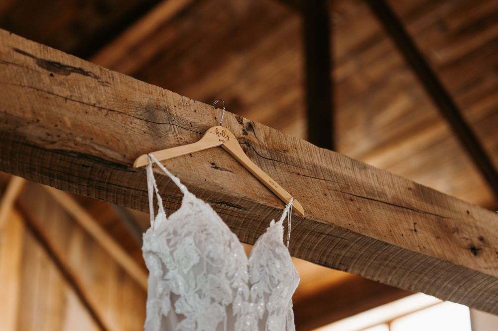 Wedding dress details showing delicate lace and straps hanging in rustic wooden room.
