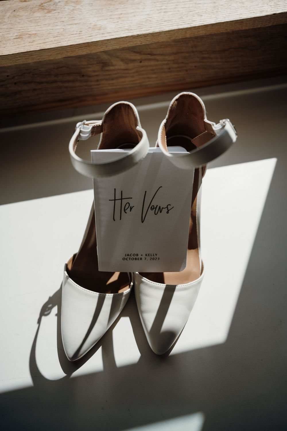 White bridal shoes with wedding vows card casting dramatic shadows in natural light.