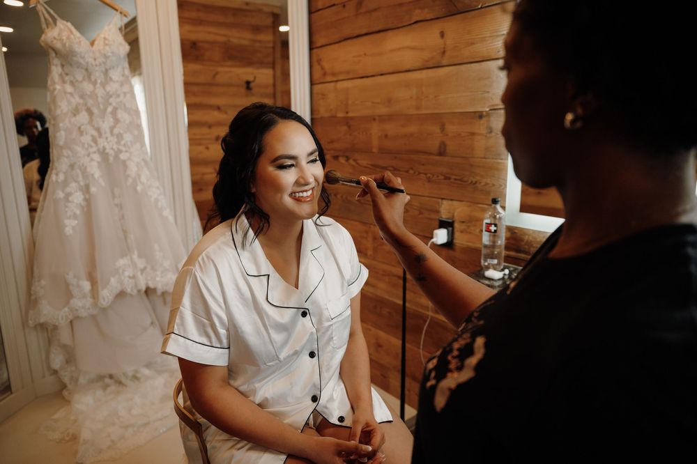Makeup artist applies cosmetics to a client in a rustic wooden cabin setting.