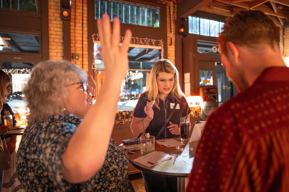 A group gathers around a wooden table in a rustic restaurant setting with exposed brick walls and wooden beams.