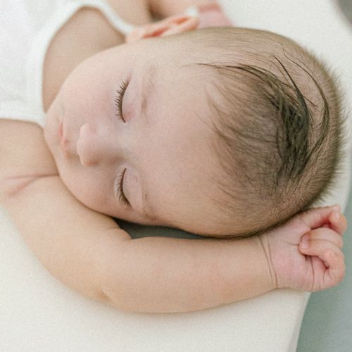 Close-up of a sleeping infant with dark hair resting peacefully against white fabric.