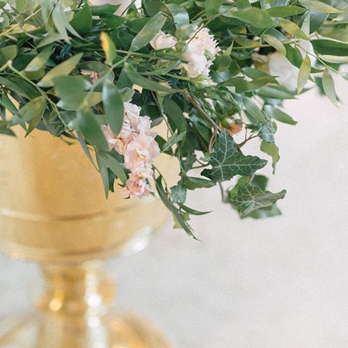 Fresh green foliage with soft pink blooms arranged in a gold metallic container.