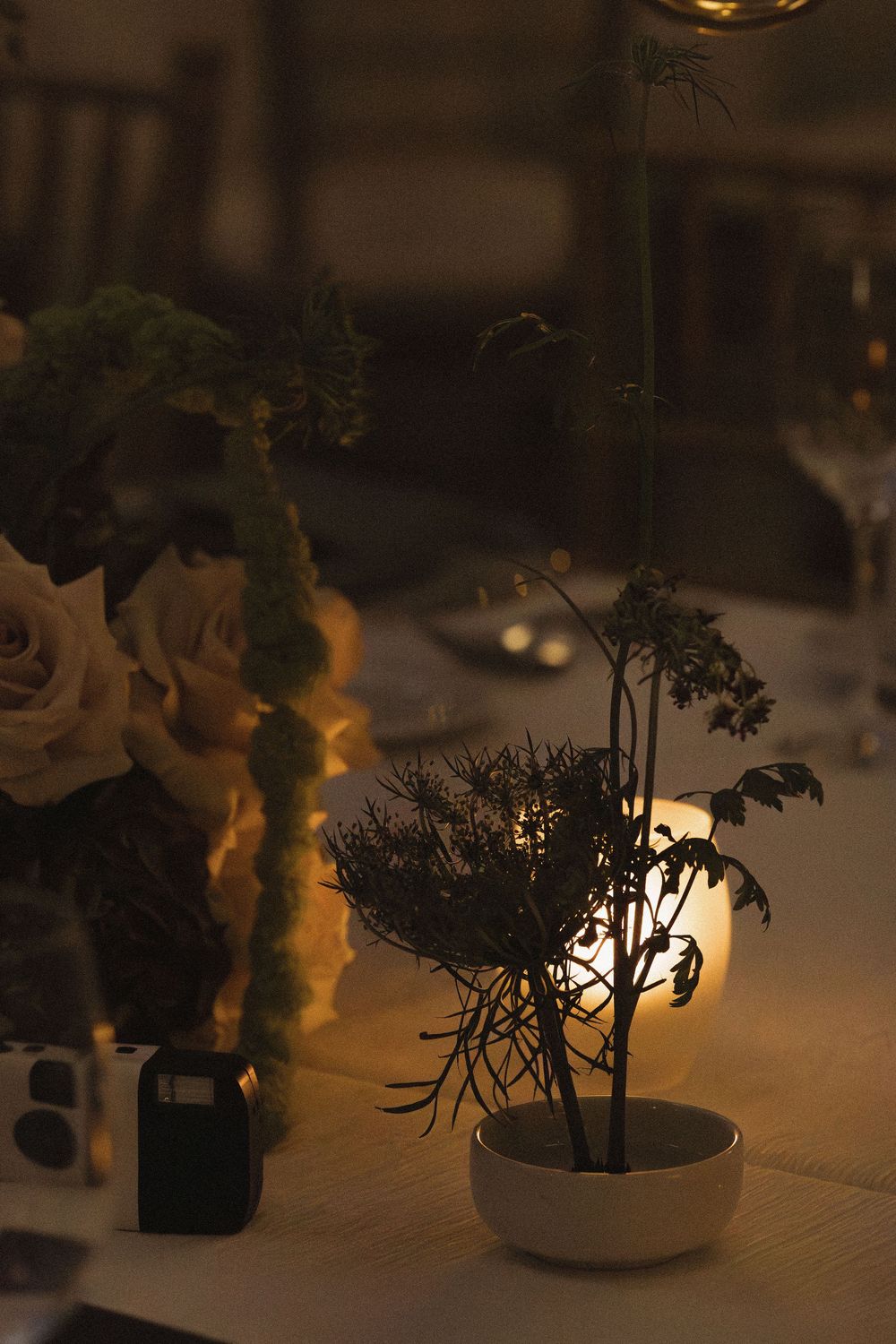 Elegant table centerpieces featuring small potted plants illuminated by warm candlelight create an intimate dining atmosphere.