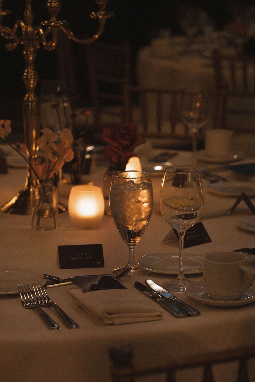 An elegant table setting at a wedding reception with candlelight, wine glasses, and place settings in warm ambient lighting.