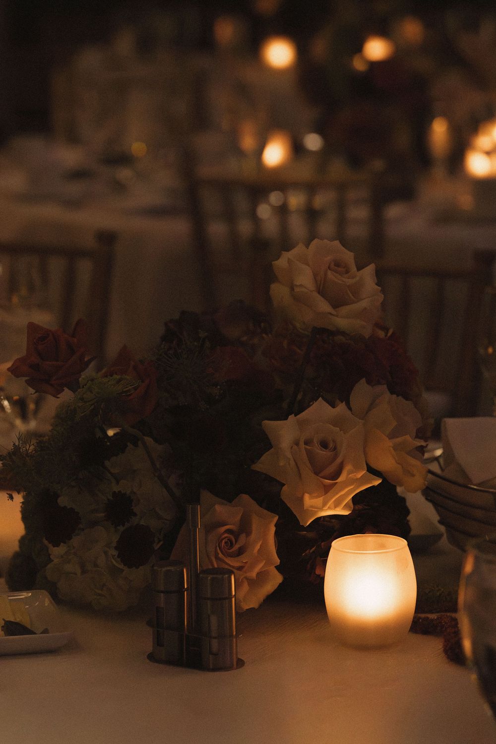 Romantic candlelit table decorations with white roses and greenery create a soft, ambient glow for an evening event.