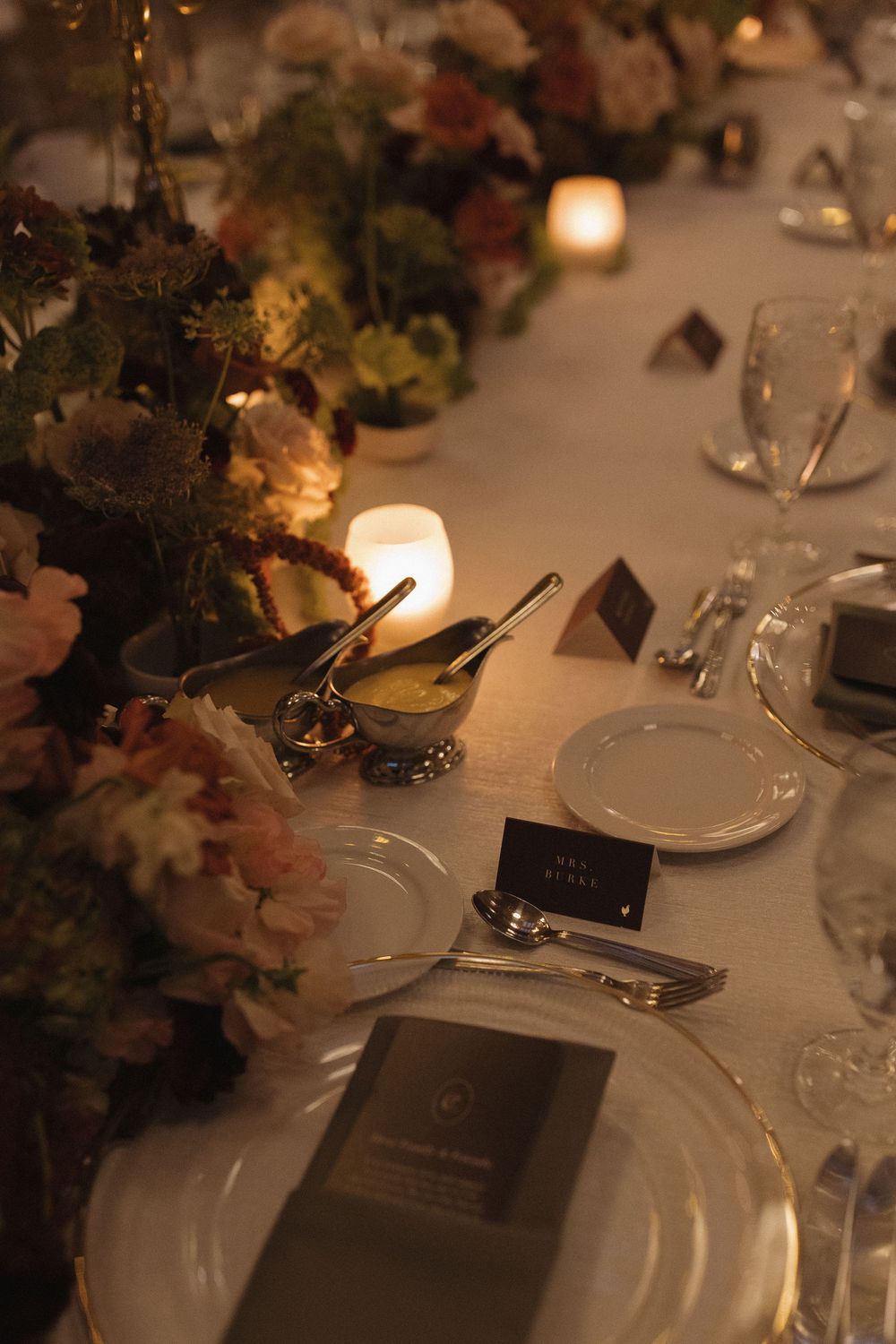 Elegant wedding reception table setting with glowing candles, floral arrangements, and place settings in warm lighting.
