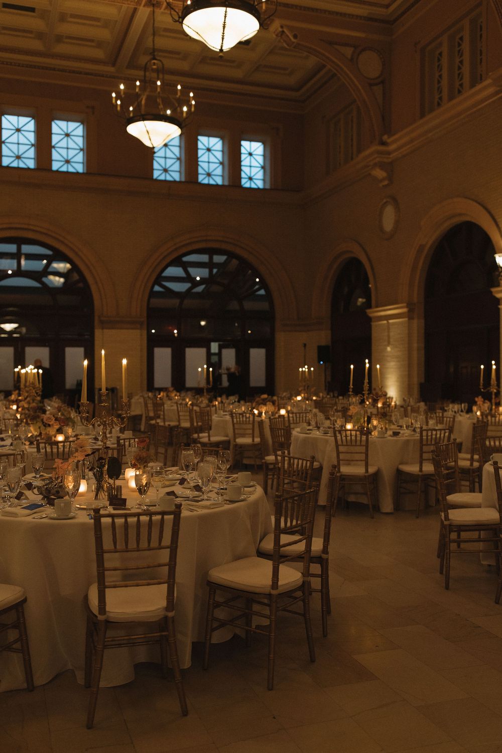 Elegant ballroom set for a formal dinner with round tables, chandeliers, and ornate architectural details.