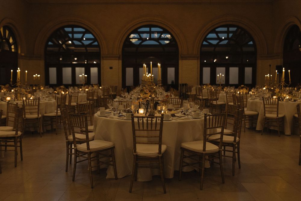 Elegant wedding reception venue with round tables, golden lighting, and crystal chandeliers creating a romantic ambiance.