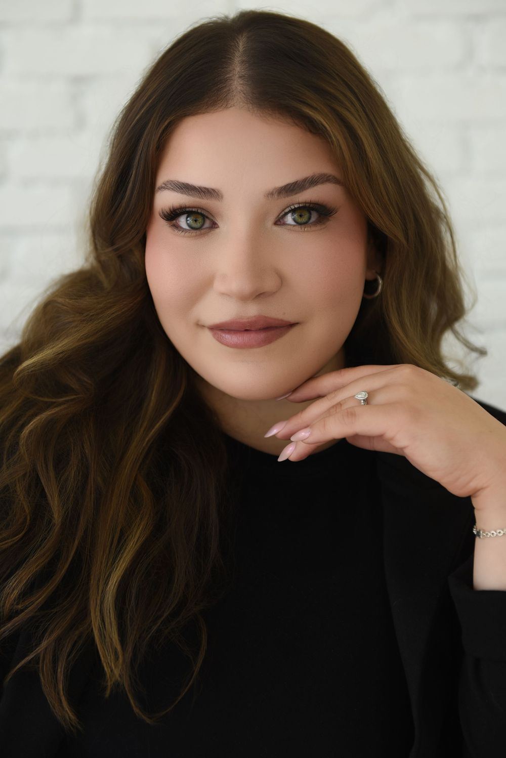 Portrait series of a person in a black top with wavy brown hair and natural makeup against a light background.