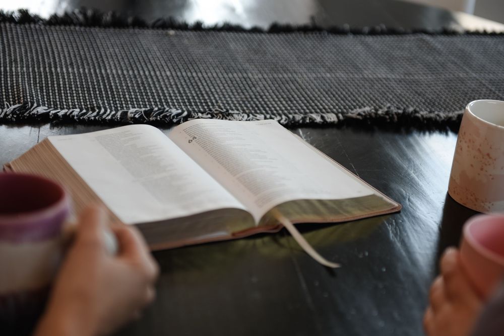 A close-up view of hands holding and reading from an open Bible with text visible on the pages.