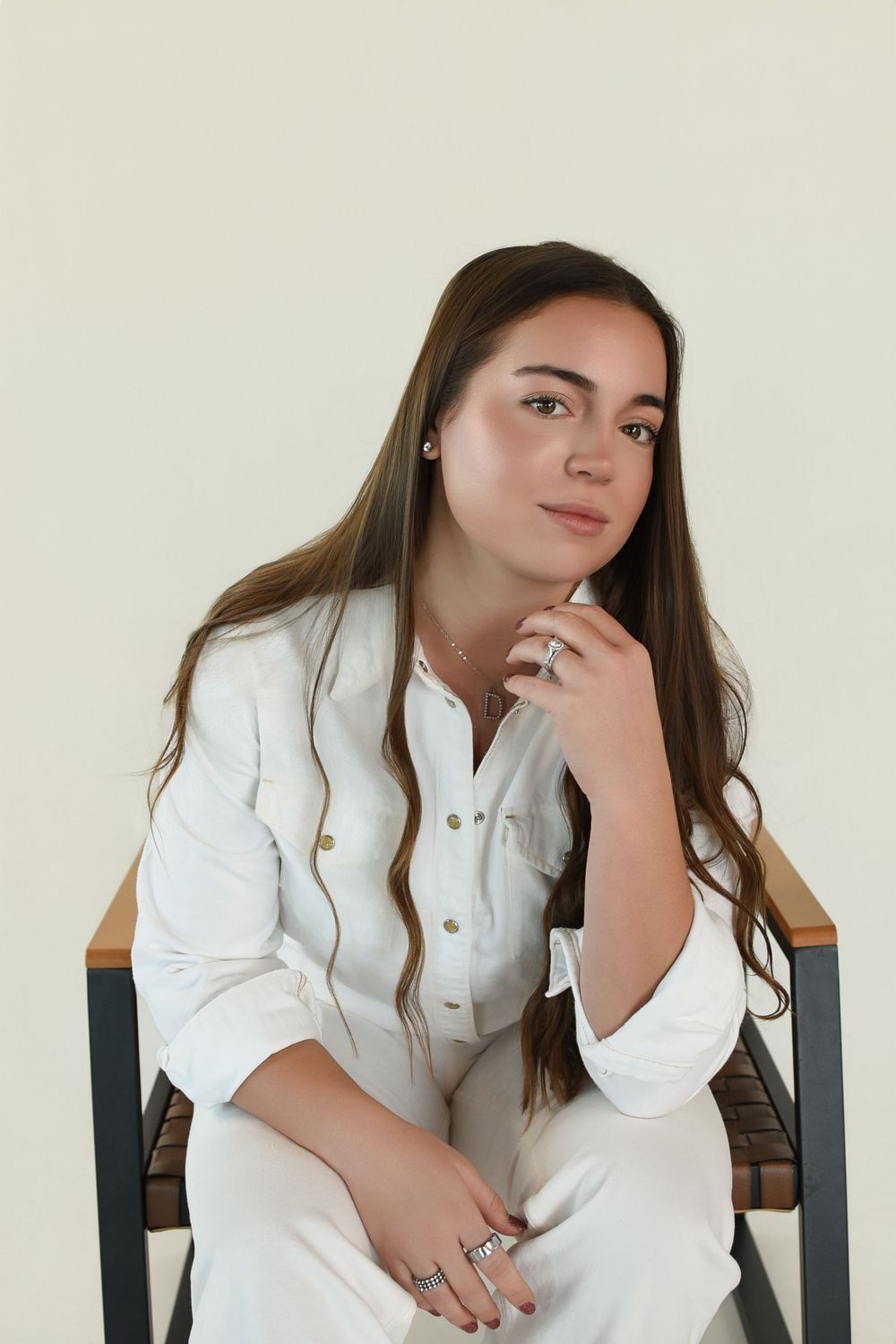 A person in a white button-down shirt poses thoughtfully while sitting in a dark chair.