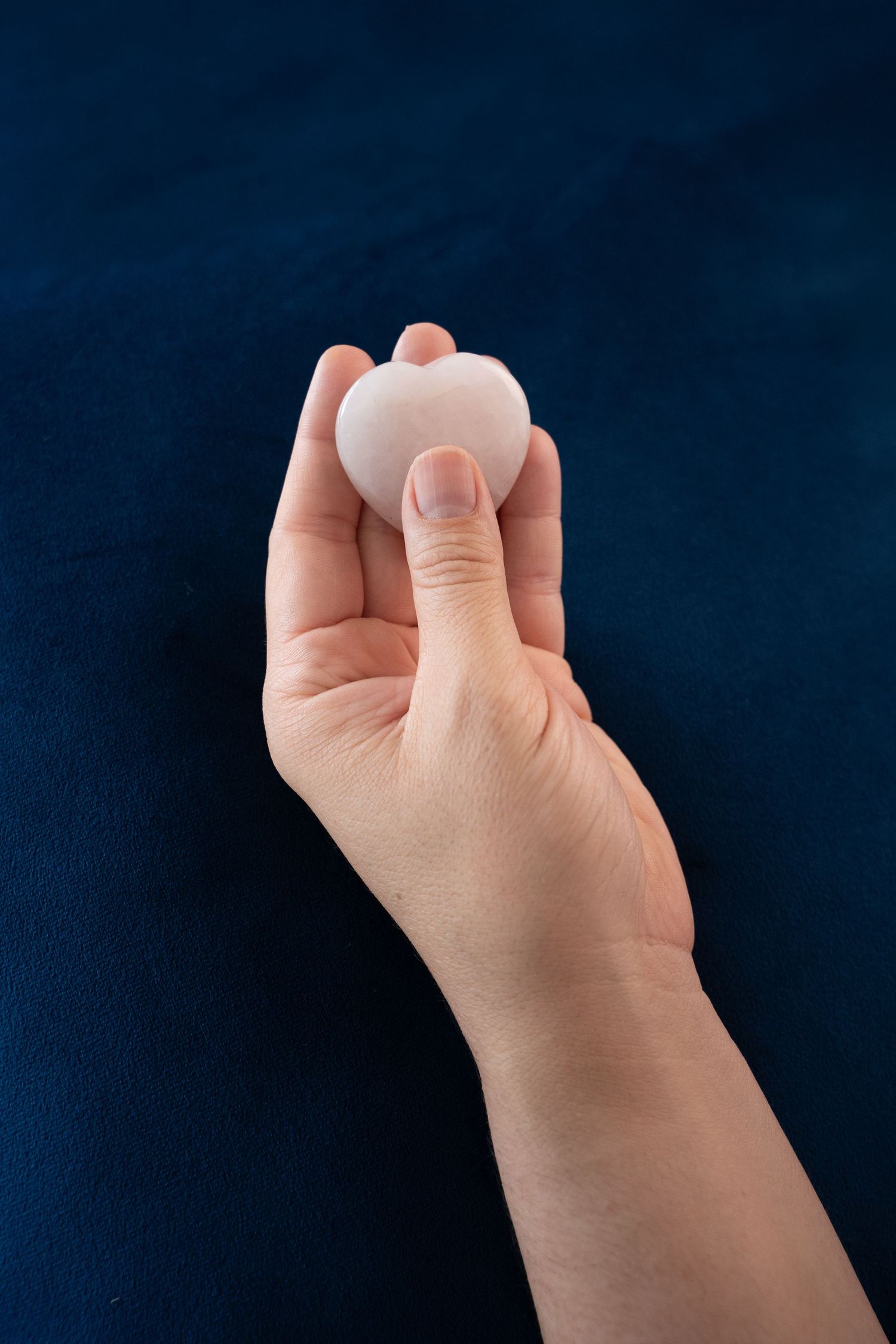 A hand holding a small white egg against a dark navy blue background.