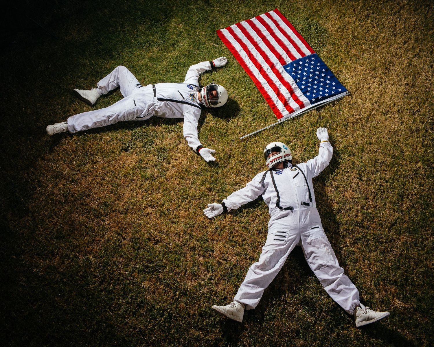 Astronaut suits lying on grass with American flags in an artistic installation.