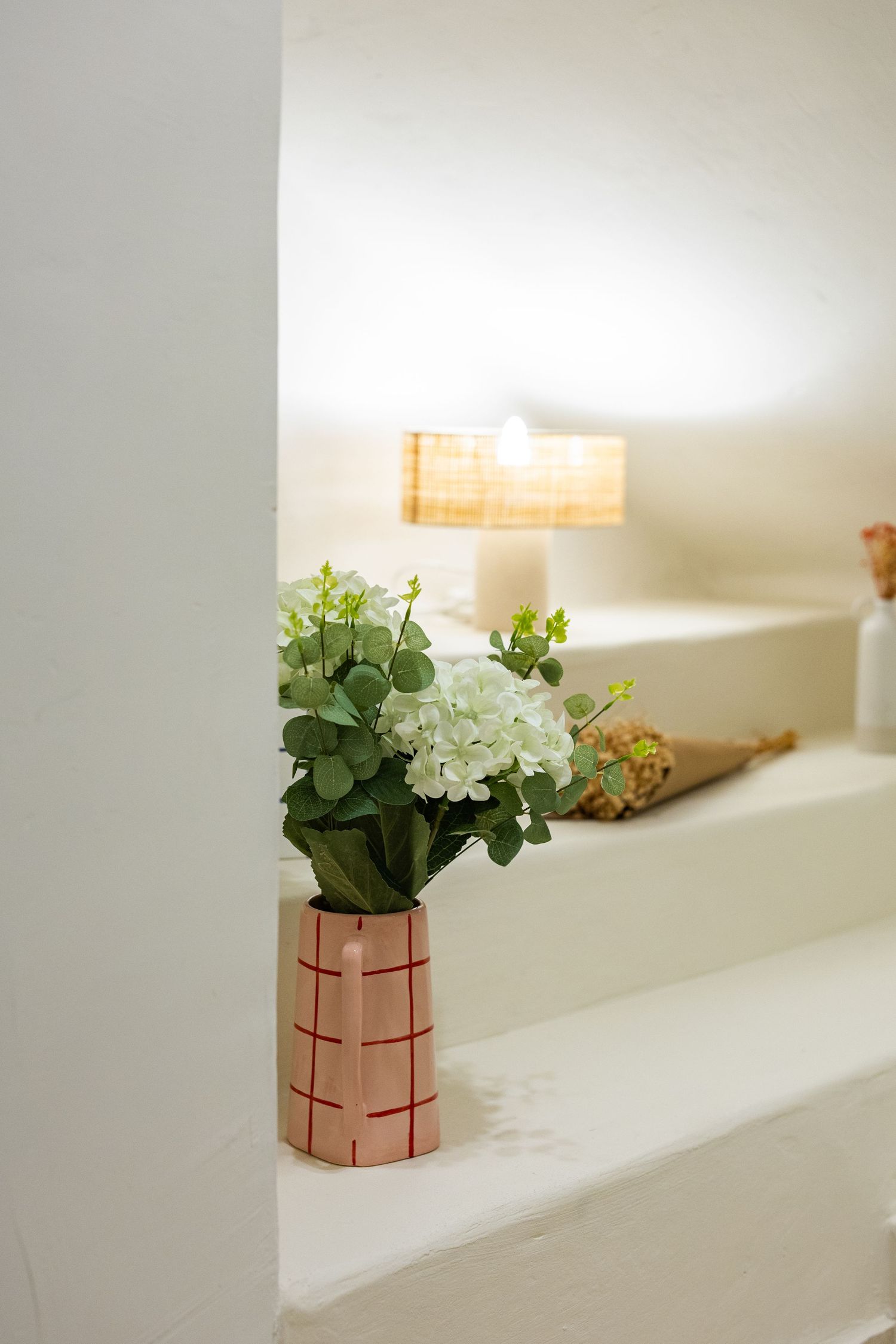 Small green plant with white flowers arranged in a modern copper-colored geometric planter on a white windowsill.