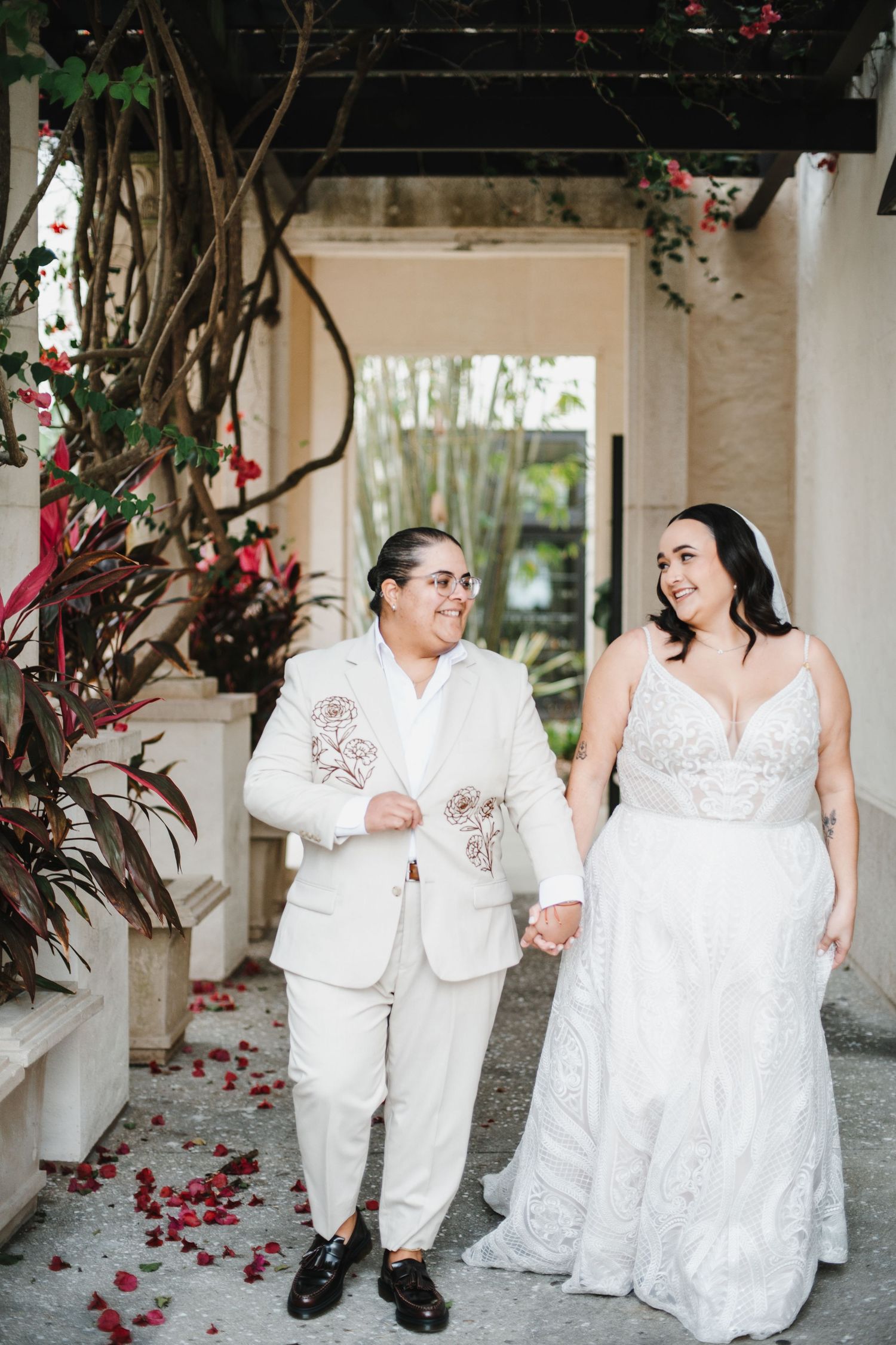 A couple in matching white outfits shares a tender moment in an outdoor venue decorated with red rose petals.