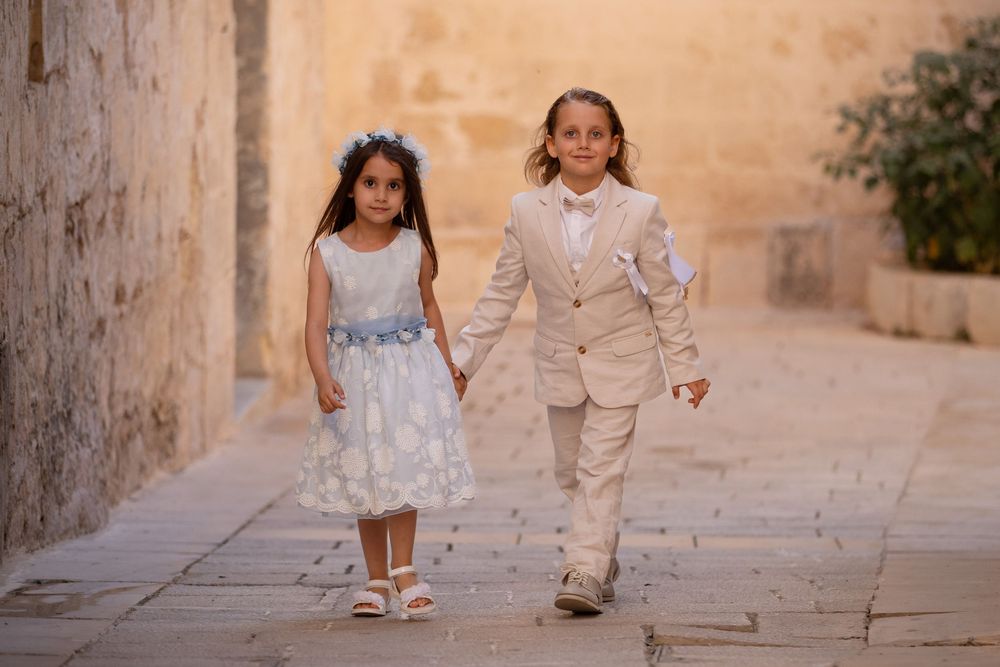 Two children walking together on a stone path in formal attire.