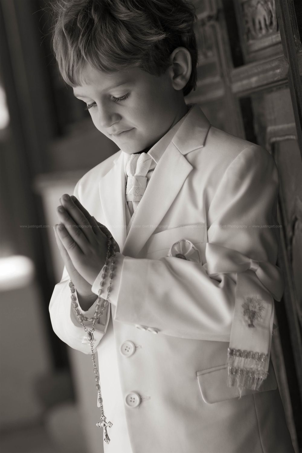 Black and white photos of a young child in white formal attire praying.