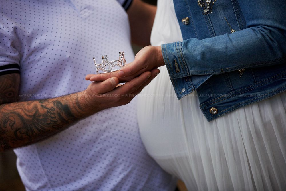 Close-up of hands with tattoo and jewelry against white maternity dress.