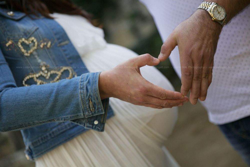 Hands gently touching a pregnant belly in white dress with denim jacket detail.