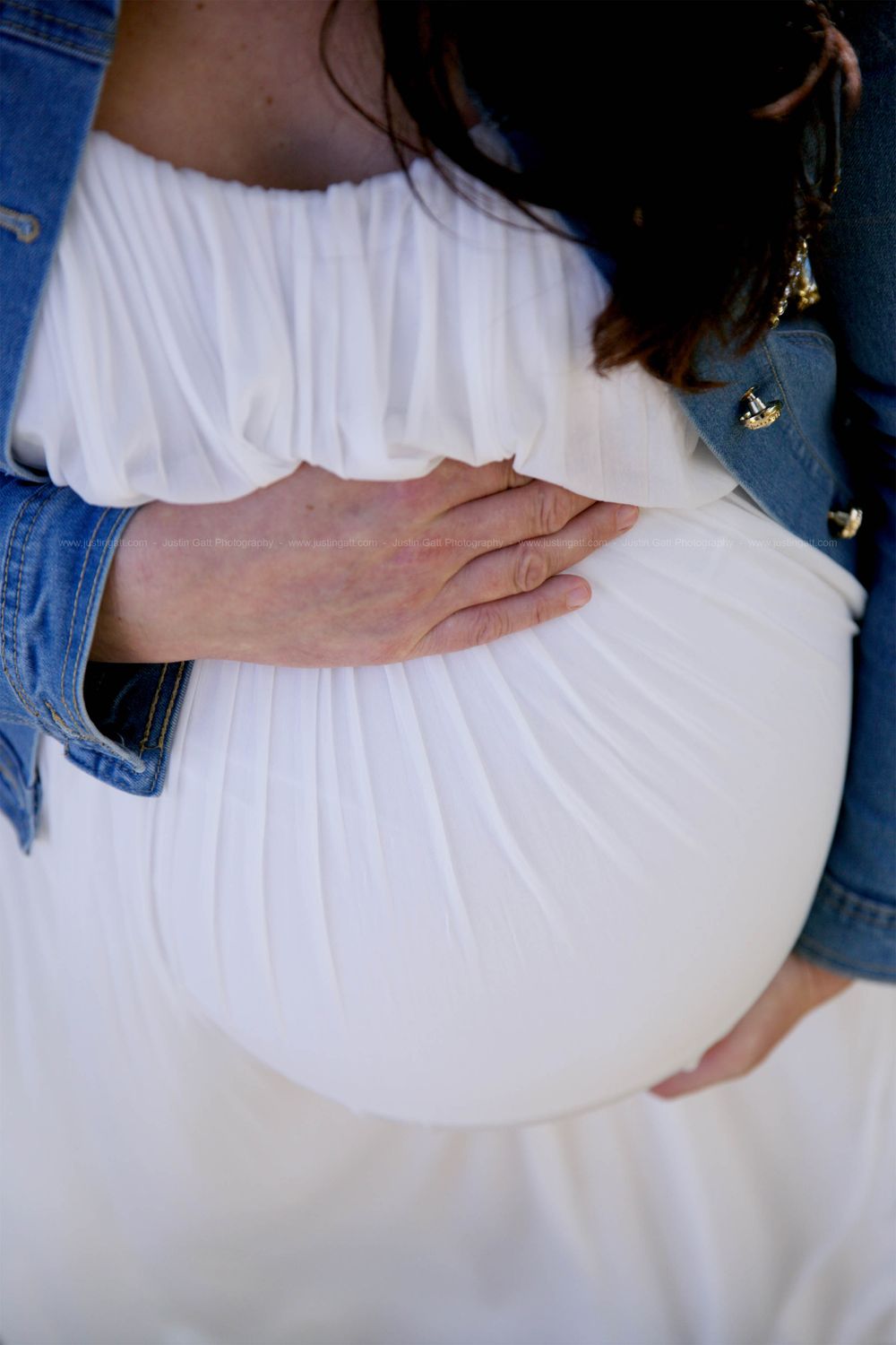 Close-up of hands tenderly cradling a pregnant belly in flowing white dress.